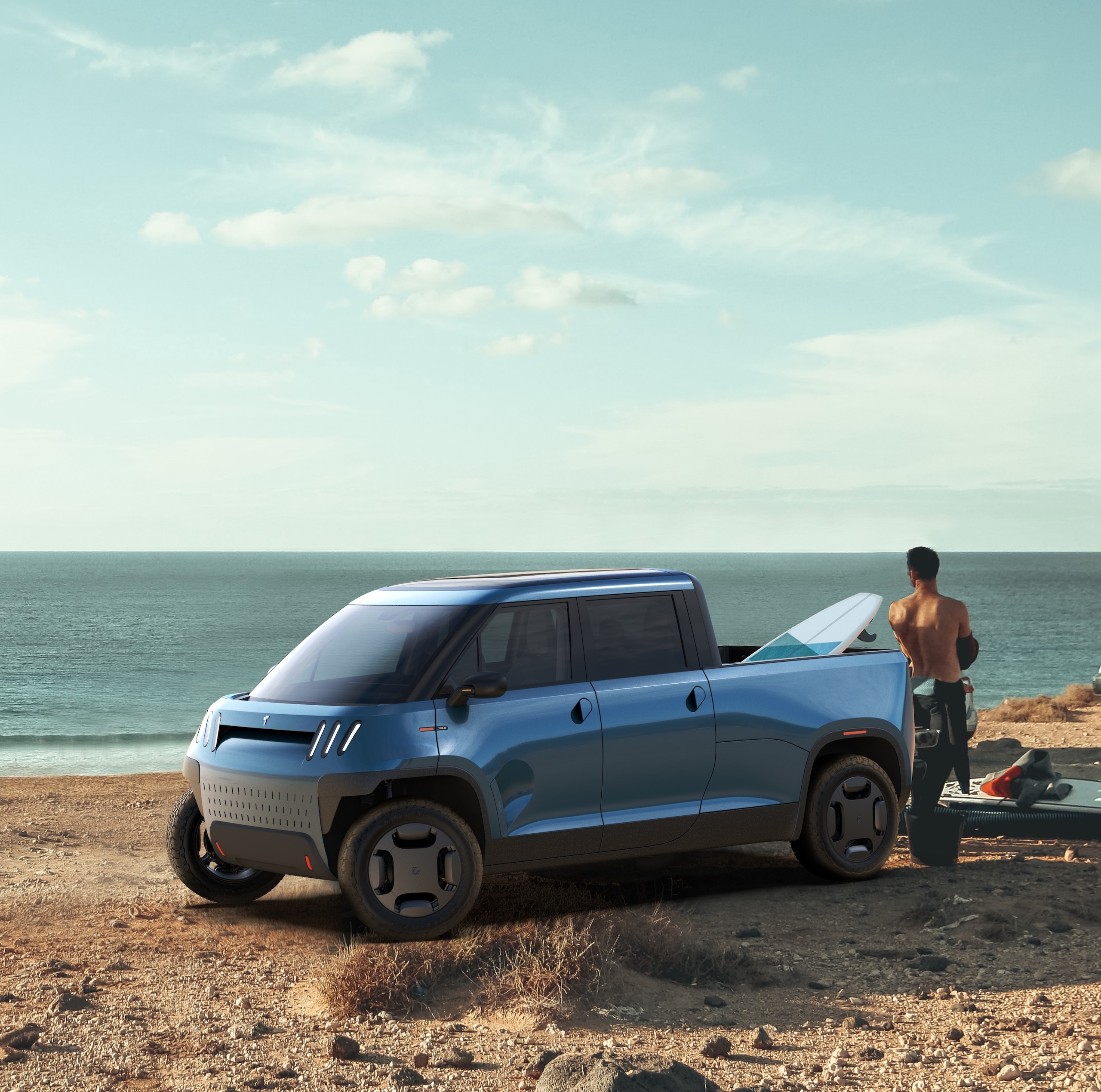Blue TELO truck on a beach with a surfboard in the bed and a surfer looking at the ocean.